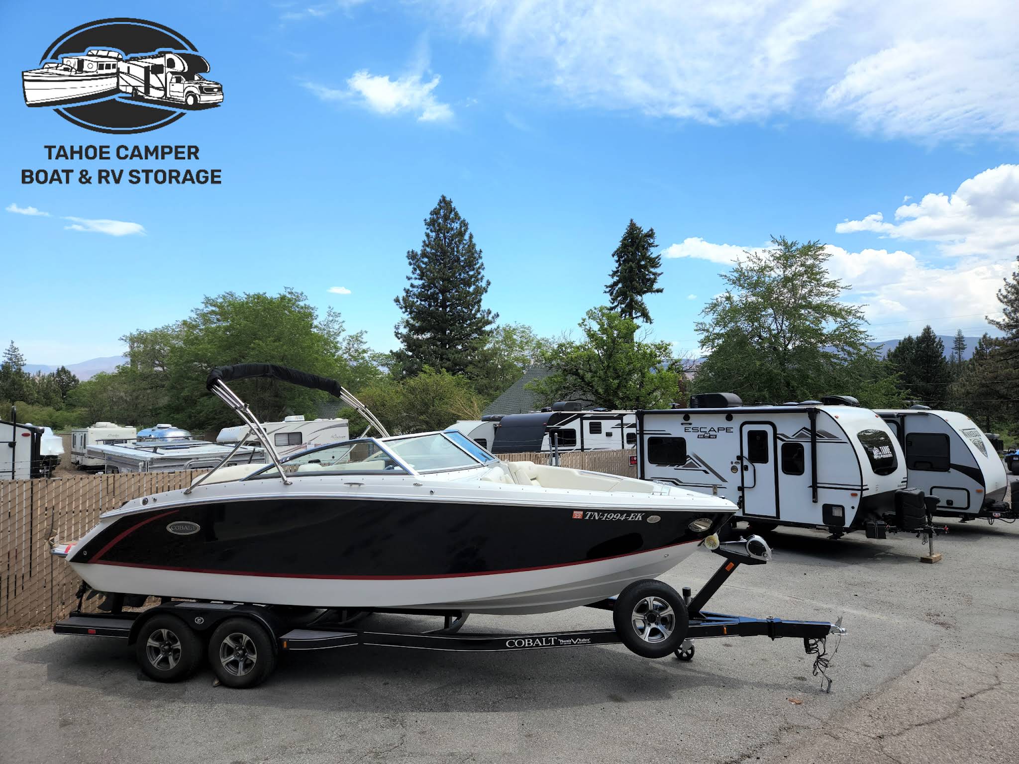 Boat in the foreground with RVs and travel trailers behind it at Tahoe Camper Storage, with the business logo in the upper left